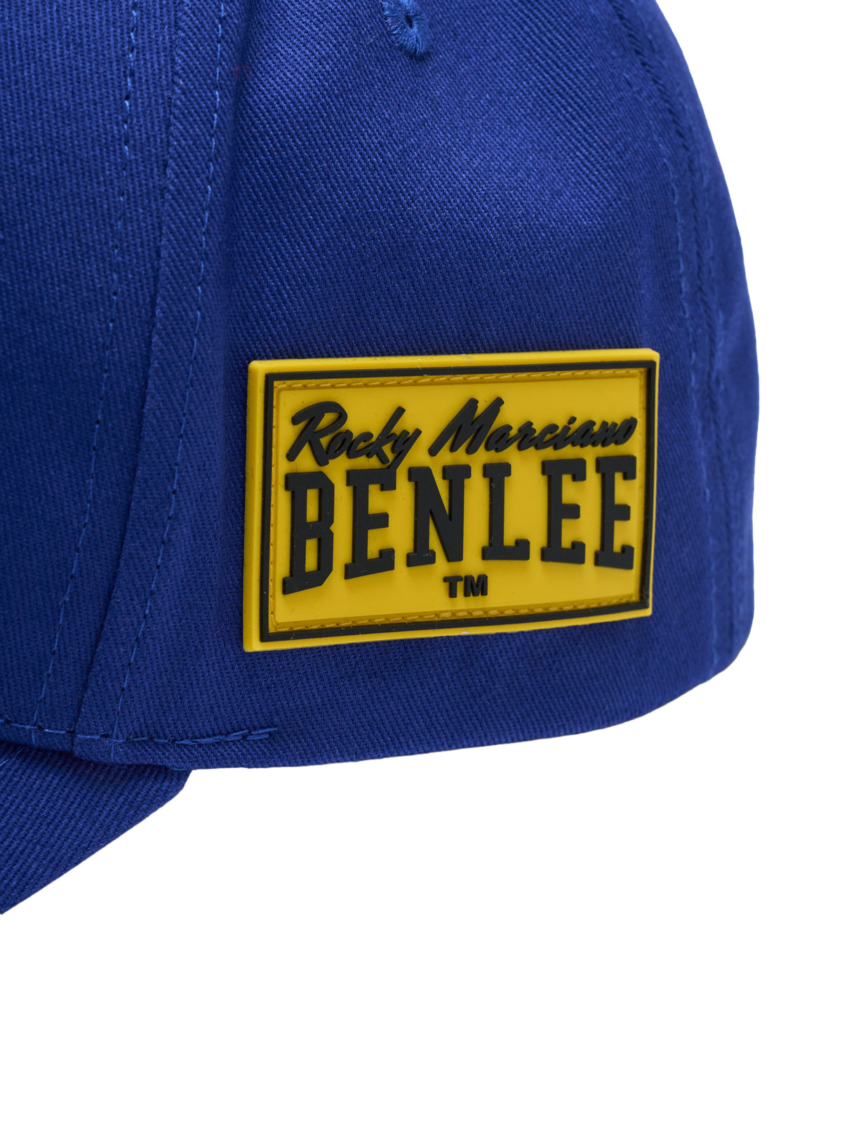Nahaufnahme eines gelben Gummi-Patches mit dem schwarzen Logo „Rocky Marciano BENLEE TM“ auf einer blauen Kappe.