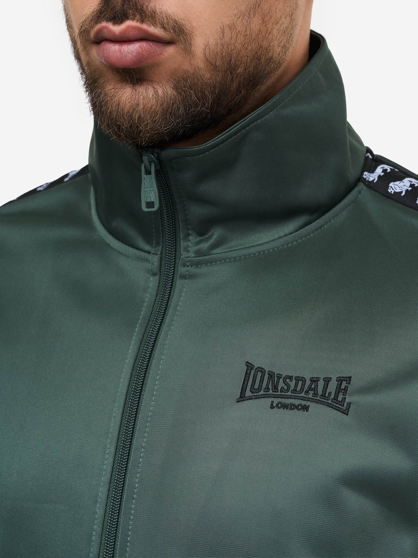 Detail: Lonsdale Logo-Stickerei und Reisserschlusstasche am Wyberton Trainingsanzug Oliv