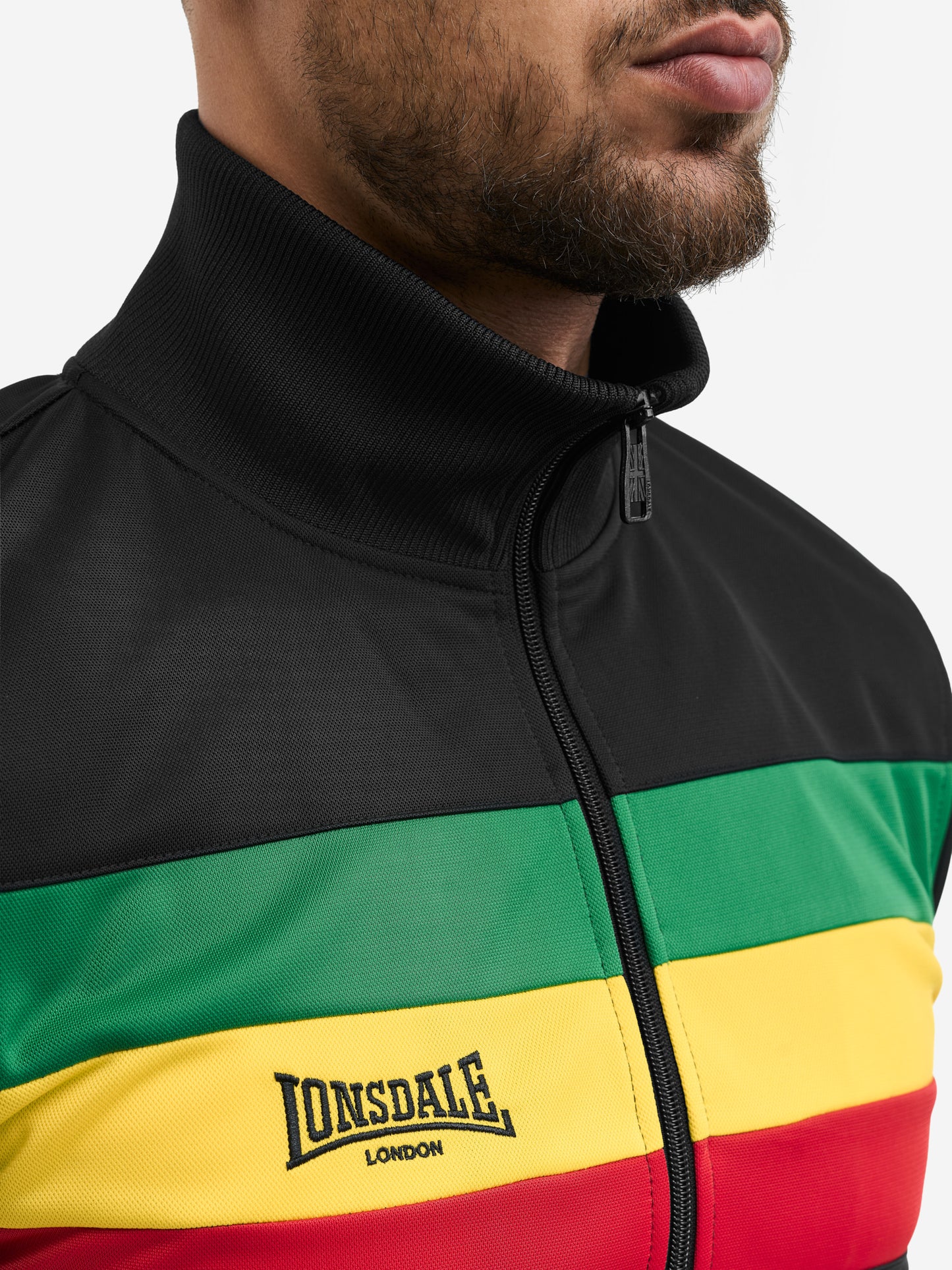 Detail der Lonsdale Trainingsjacke: Regenbogen-Bruststreifen und gesticktes Logo auf schwarzem Trikot-Fleece