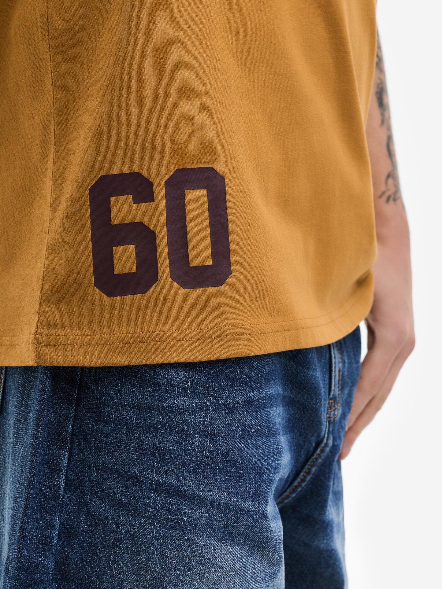 Detail des Lonsdale T-Shirts in Ocker: Dunkler „60“ Print am unteren Saum auf hochwertigem Baumwoll-Jersey.