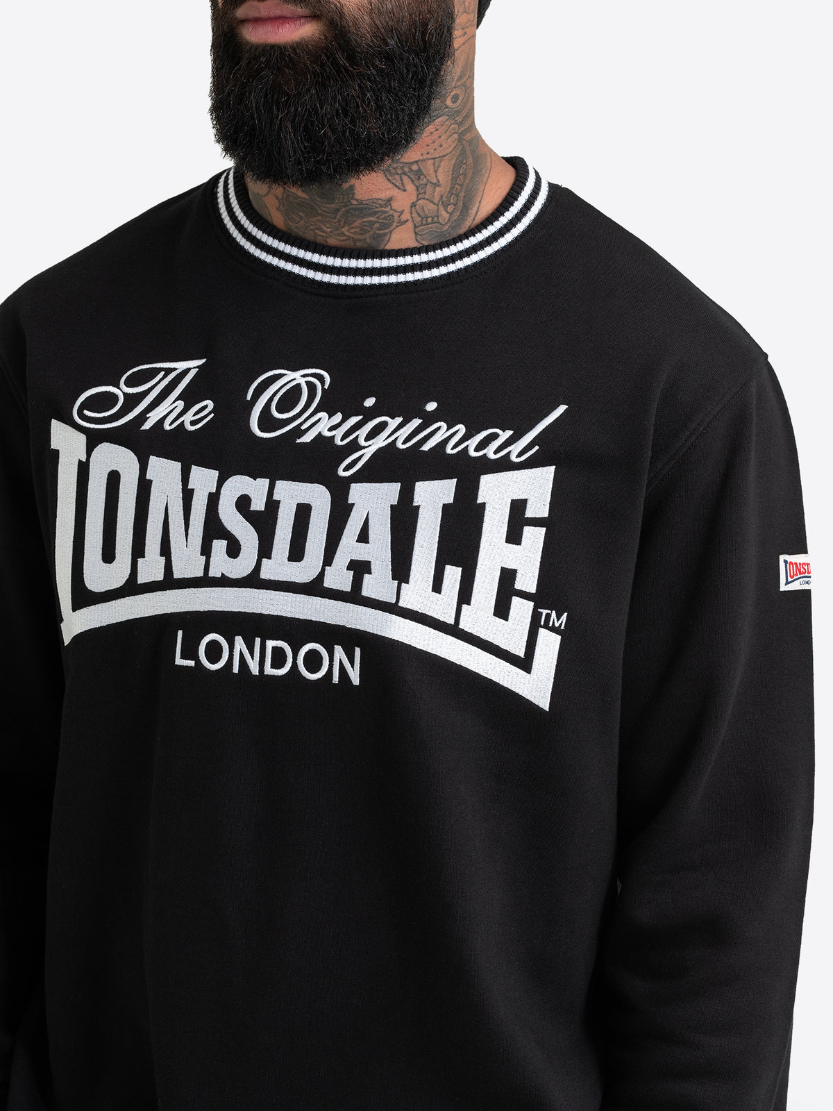 Nahaufnahme der grossen weissen Lonsdale Logo-Stickerei auf dem schwarzen Herren-Sweatshirt.
