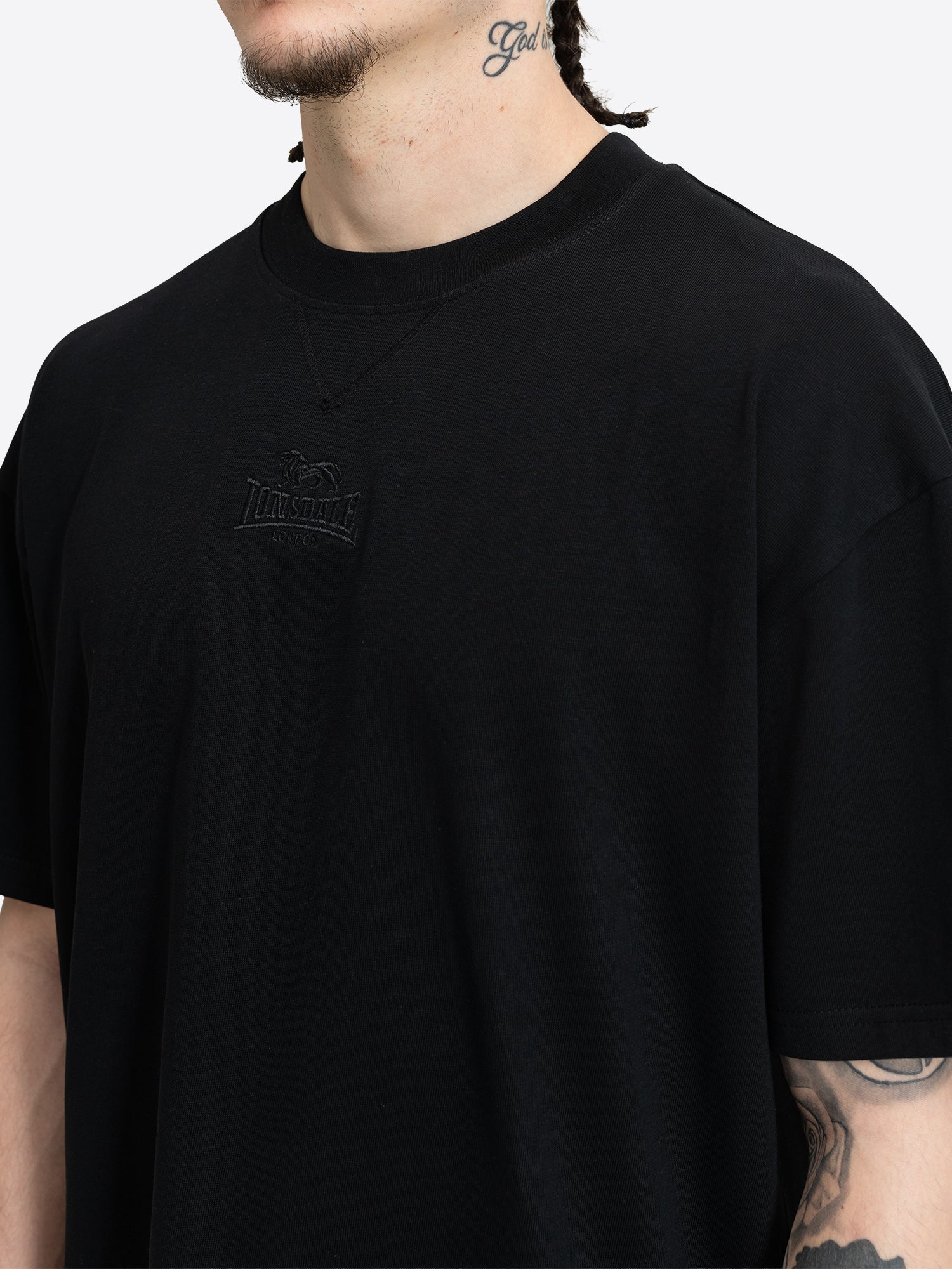 Nahaufnahme der schwarzen Ton-in-Ton Lonsdale Logo-Stickerei auf der Brust des T-Shirts.