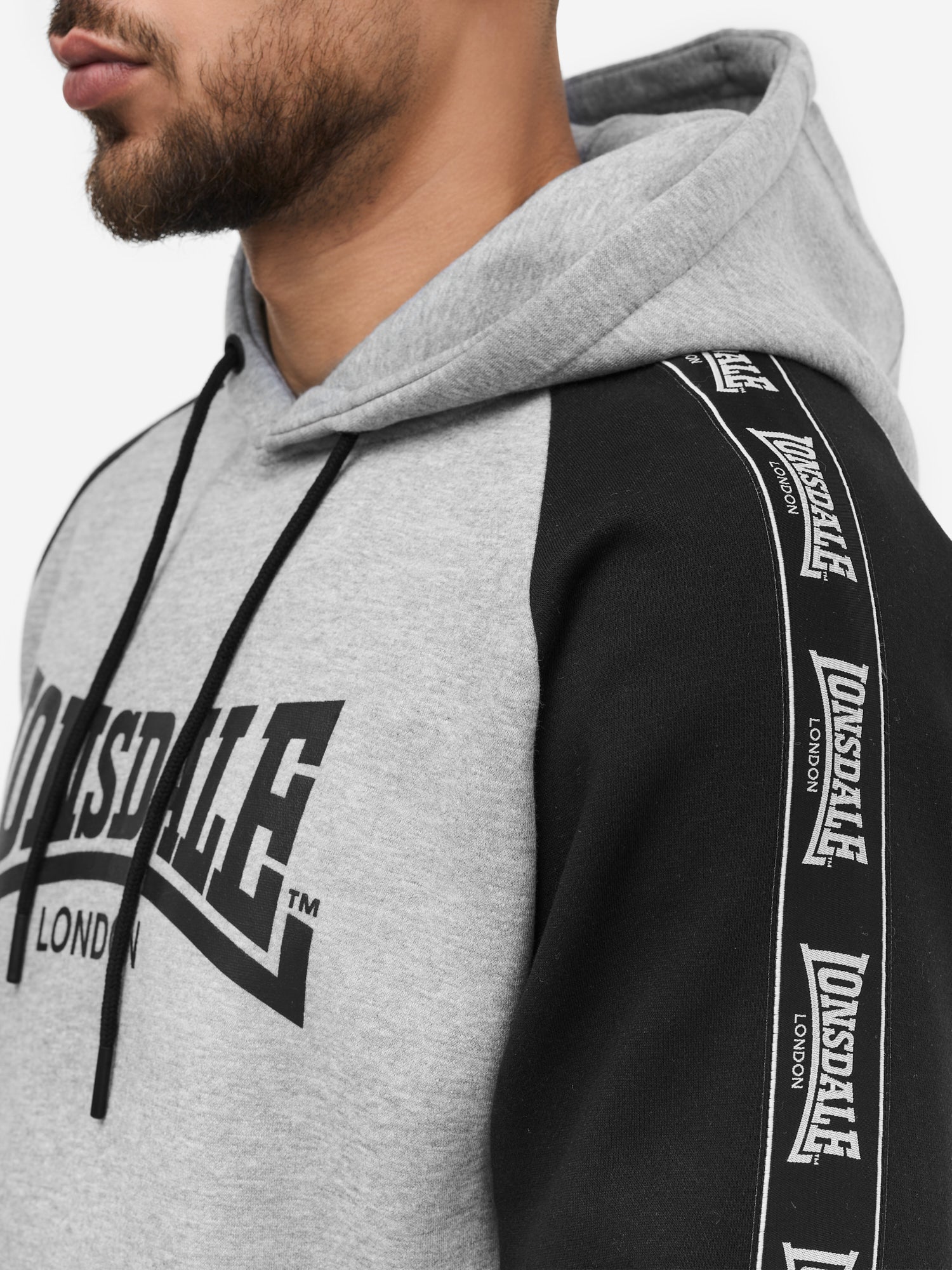 Nahaufnahme der Lonsdale Logo-Applikation und Fleece-Struktur des schwarz-grauen Jogginganzugs aus Baumwolle. 