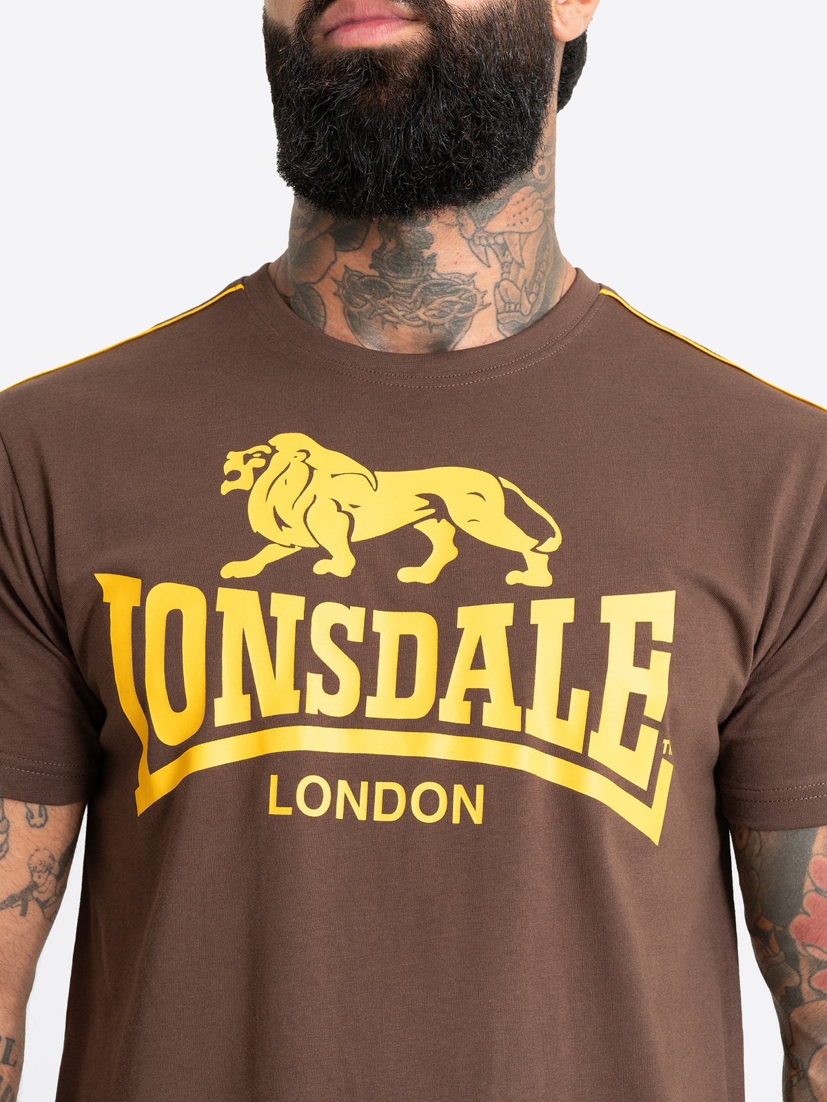 Nahaufnahme des gelben Lonsdale London Logo-Drucks auf der Brust des braunen Herren T-Shirts mit gelben Paspeln.