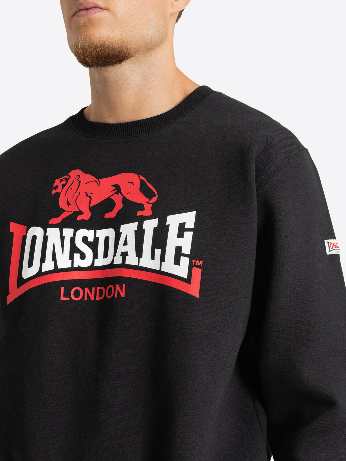 Nahaufnahme des grossen rot-weissen Lonsdale Logo-Drucks auf dem schwarzen Herren-Sweatshirt.
