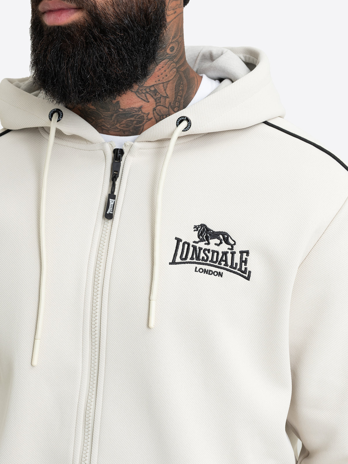 Detailansicht der Lonsdale Herren-Sweatjacke in Off-White mit Fokus auf die schwarze Logo-Stickerei und den Reissverschluss.