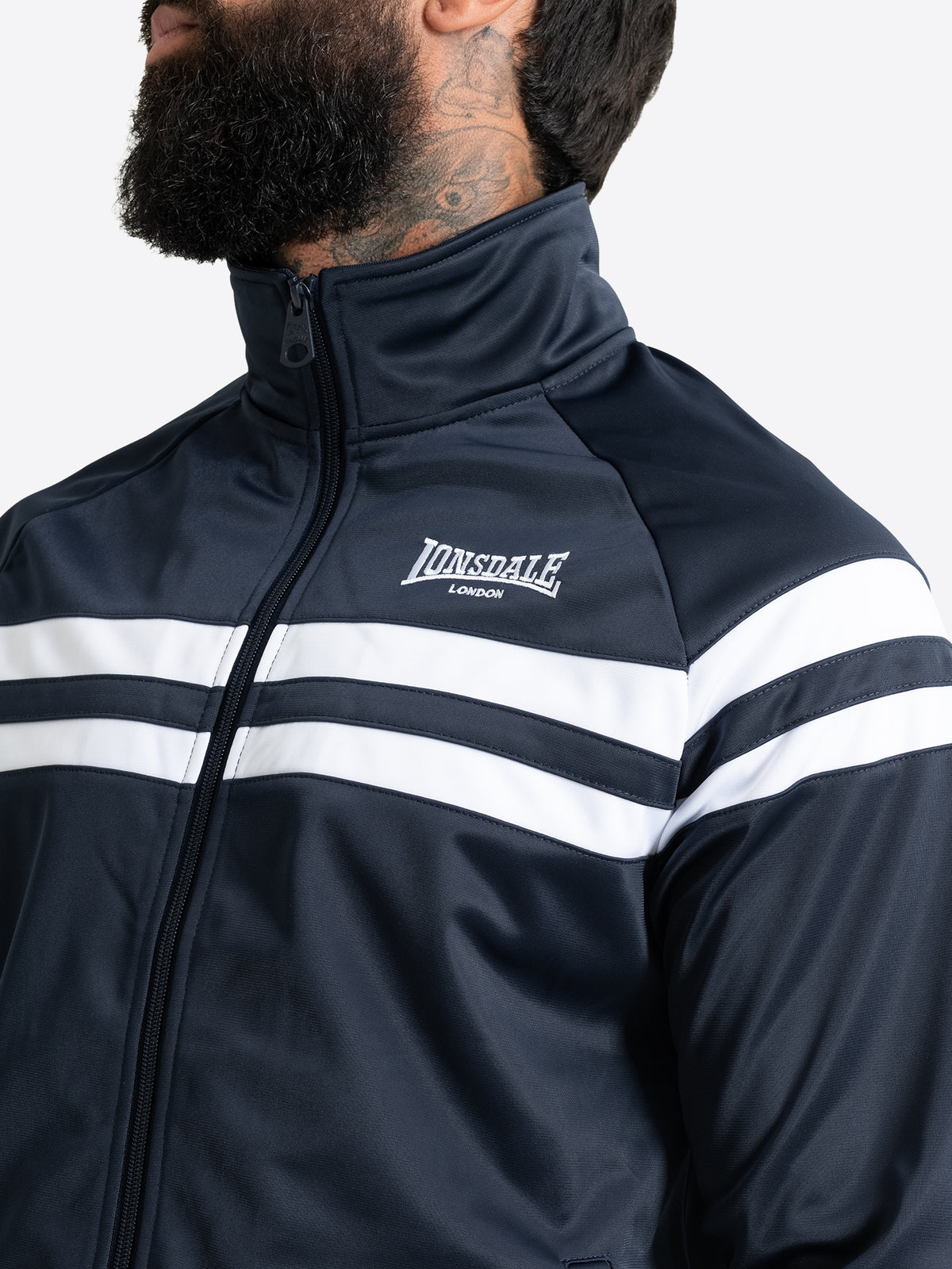 Detailansicht der Lonsdale Herren-Trainingsjacke in Dark Navy mit Fokus auf die weisse Logo-Stickerei und die Kontraststreifen.
