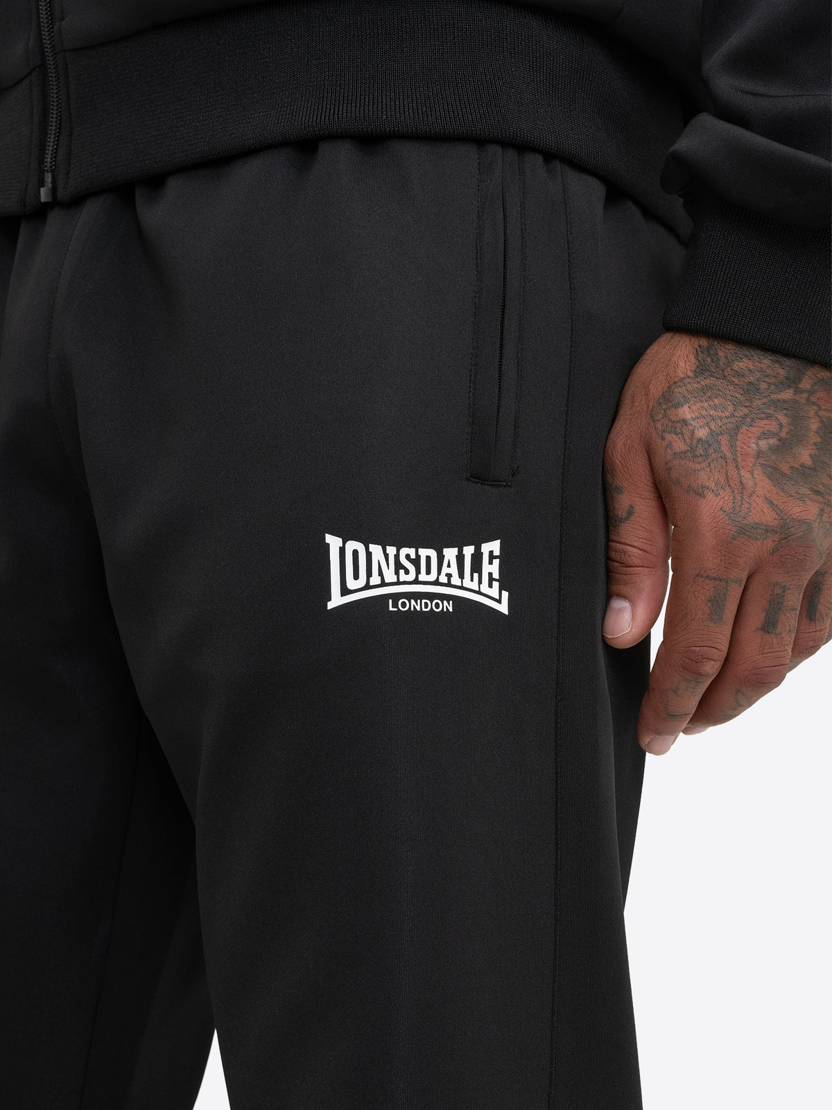 Detailansicht der schwarzen Lonsdale Jogginghose mit Logo und Reissverschlusstasche.
