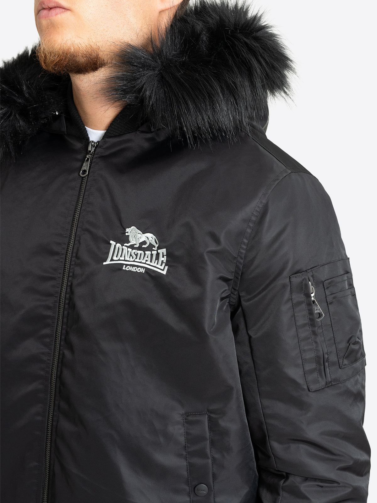 Detailansicht der Lonsdale Herrenjacke mit weissem Logo-Stick, Kunstfell und Ärmeltasche im Bomber-Stil.