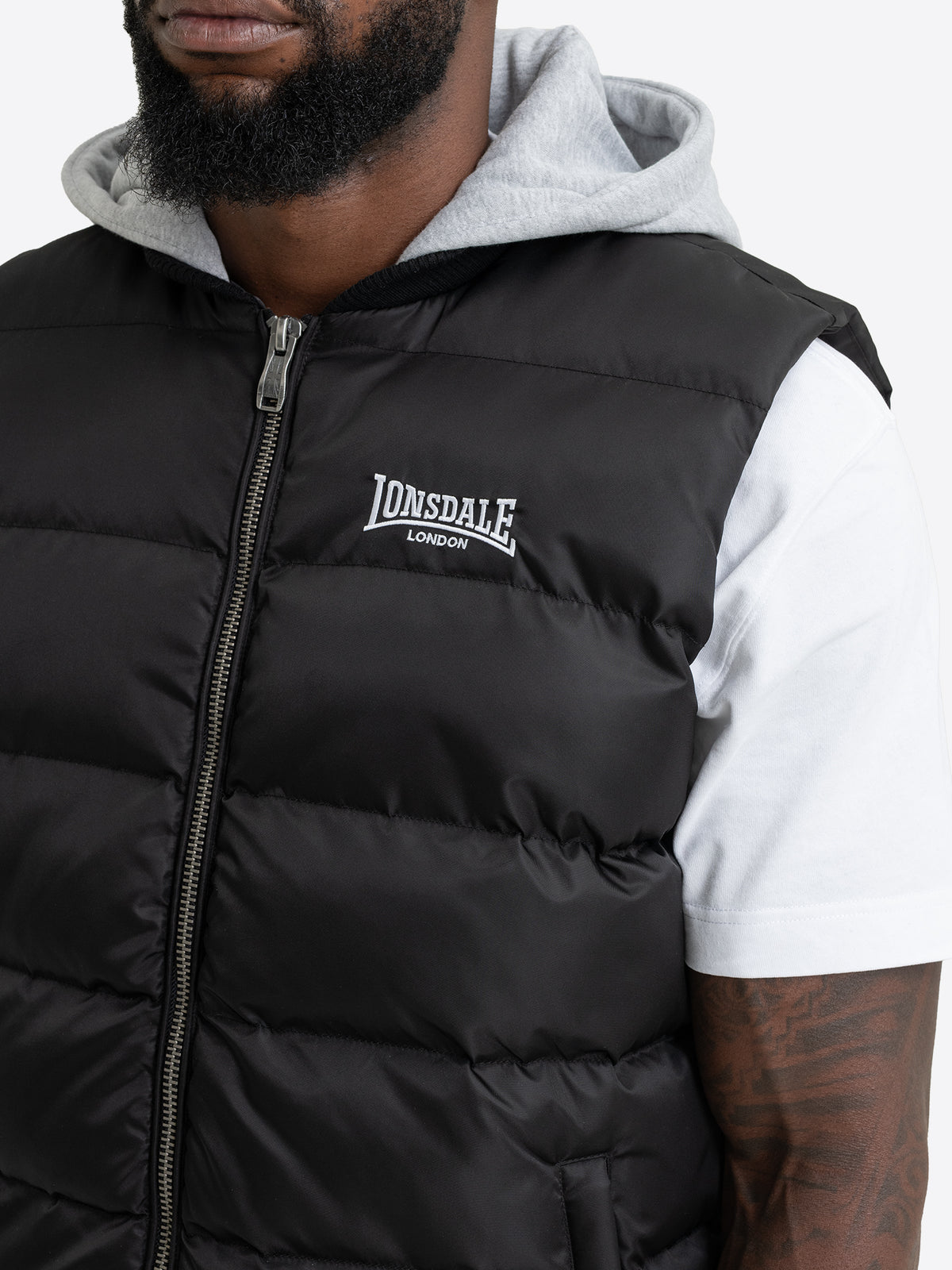Nahaufnahme der Lonsdale Herren-Steppweste mit weissem Logo-Stick auf der Brust und grauem Kapuzenansatz.