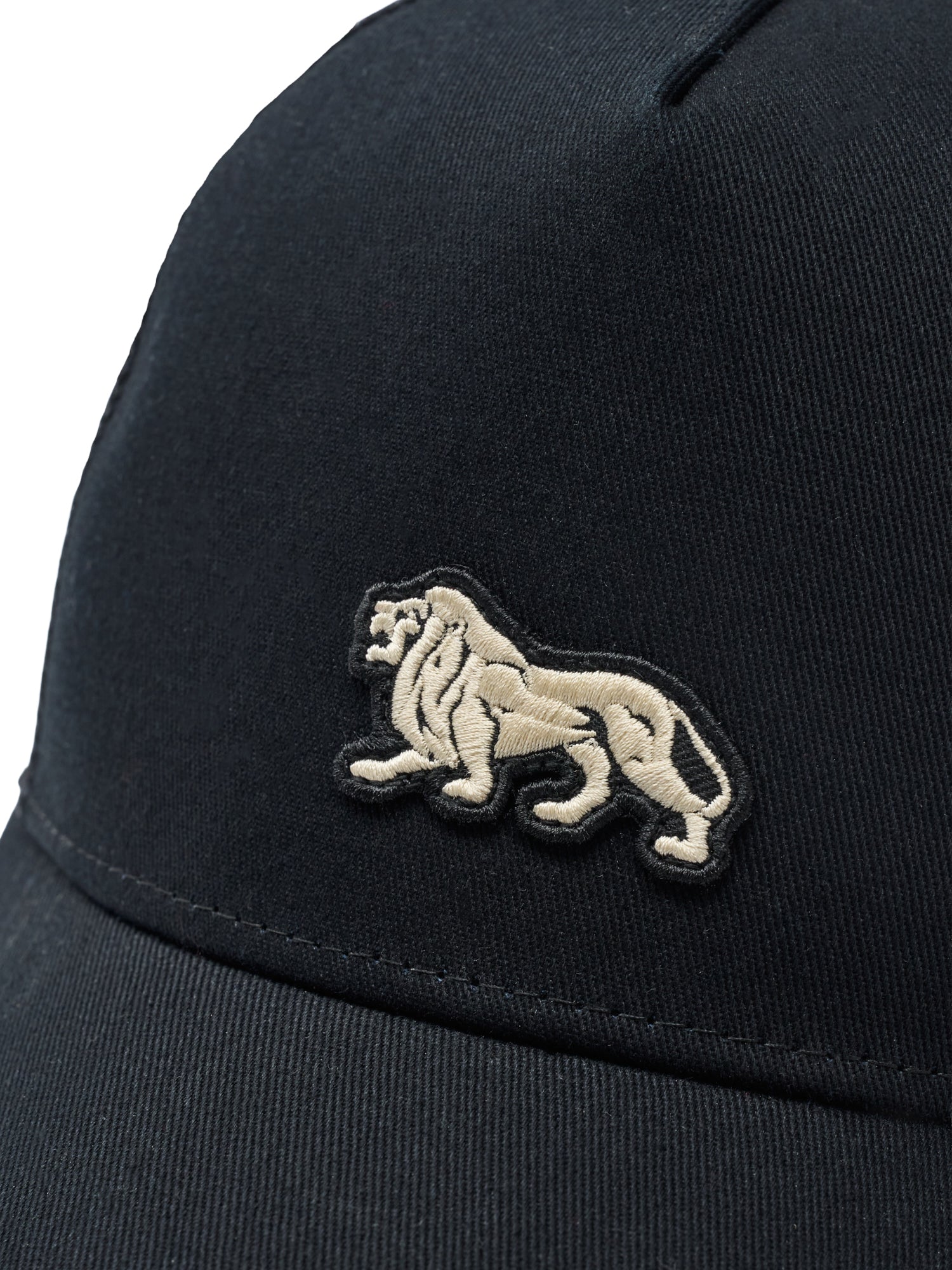 Beiger Lonsdale London Löwen-Aufnäher auf der Front einer schwarzen Trucker-Kappe. Streetwear Shop Schweiz.