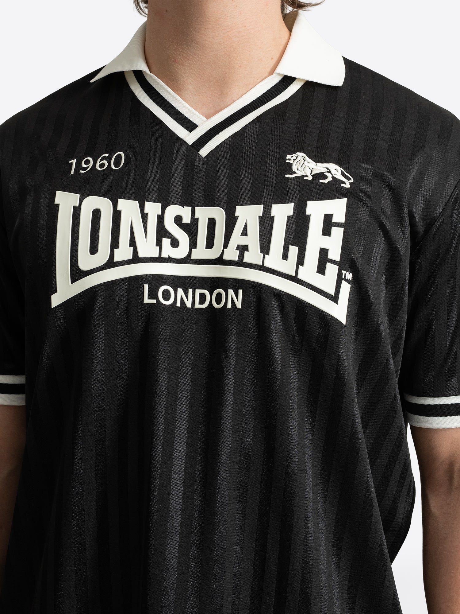 Lonsdale Unisex Trikot in Schwarz mit gestreiftem Jacquard-Muster, weissem V-Ausschnitt und Retro-Logo auf der Brust.