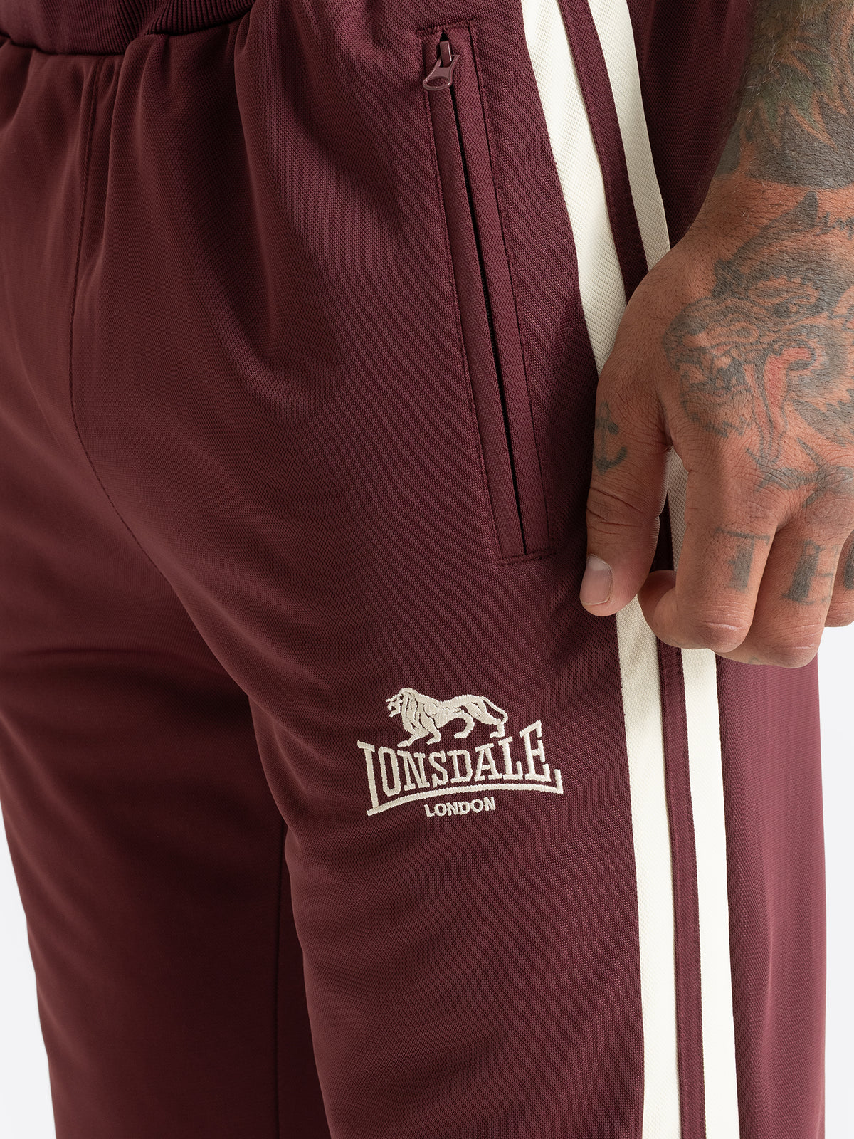 Vorderansicht der Lonsdale Herren-Trainingshose in Weinrot mit hellem Streifen und Logo.