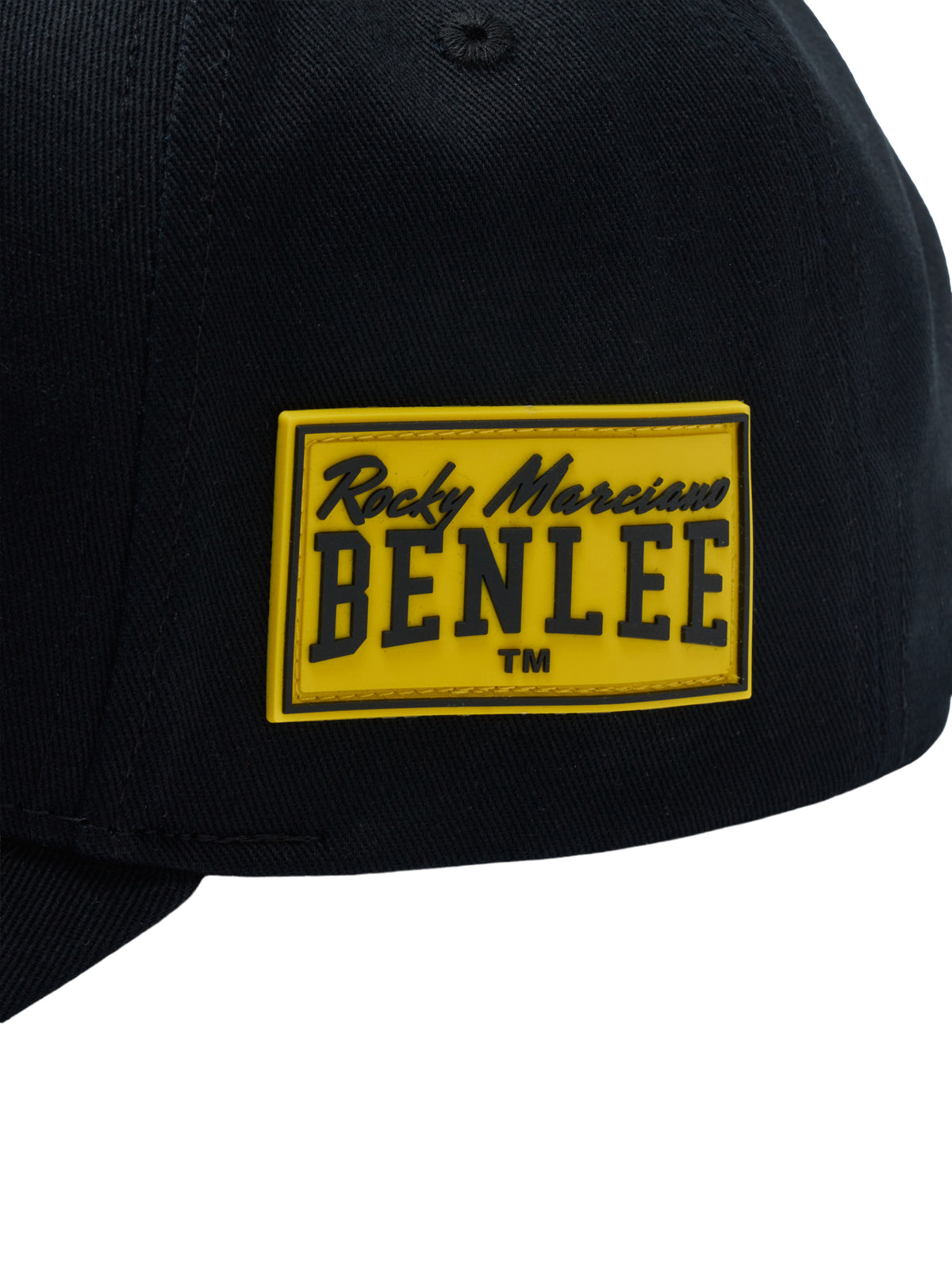 Nahaufnahme eines gelben Gummi-Patches mit dem schwarzen Logo „Rocky Marciano BENLEE TM“ auf einer schwarzen Kappe. 