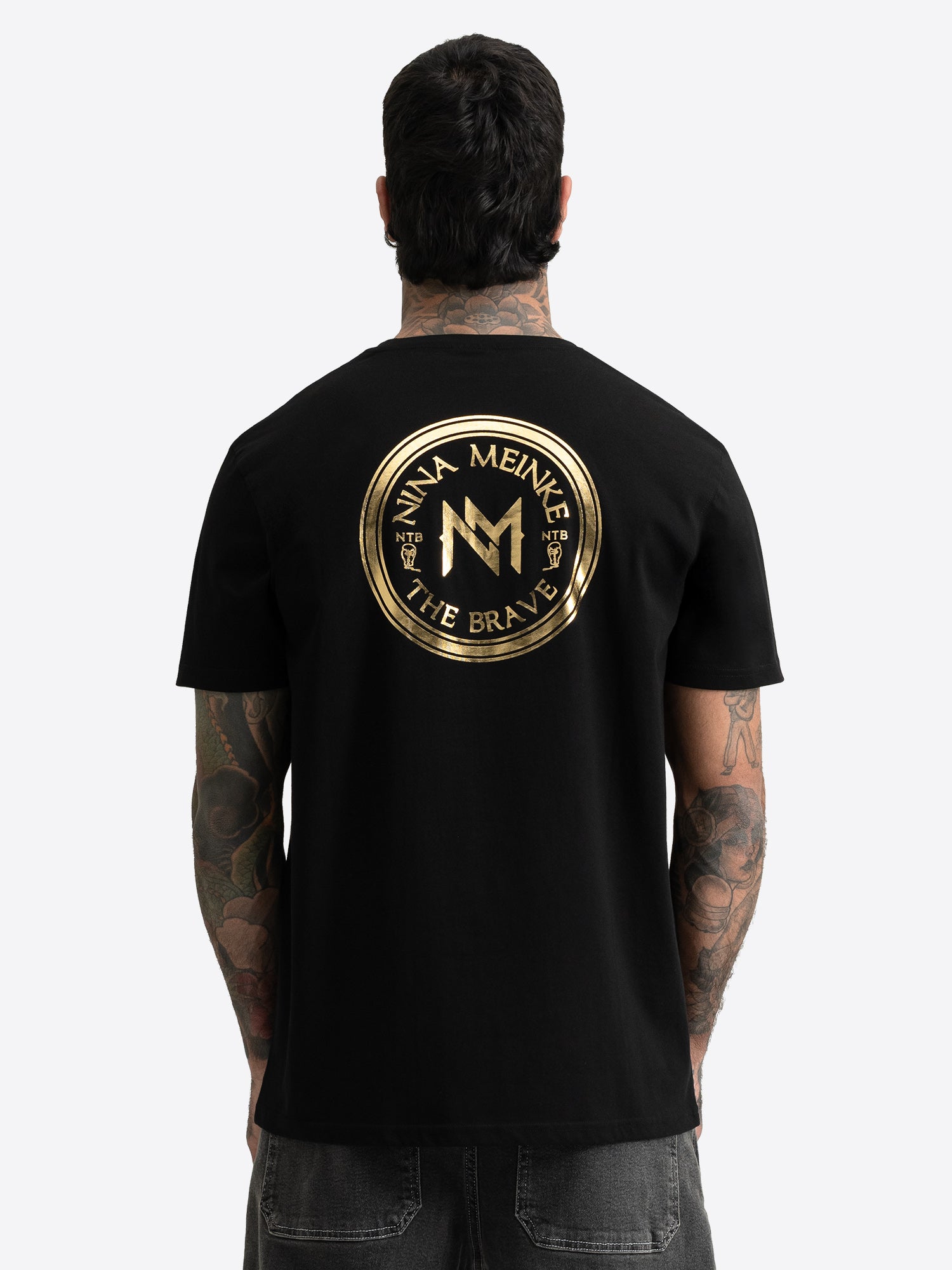 Rückseite: Schwarzes T-Shirt mit großem, rundem Nina Meinke Gold-Print.