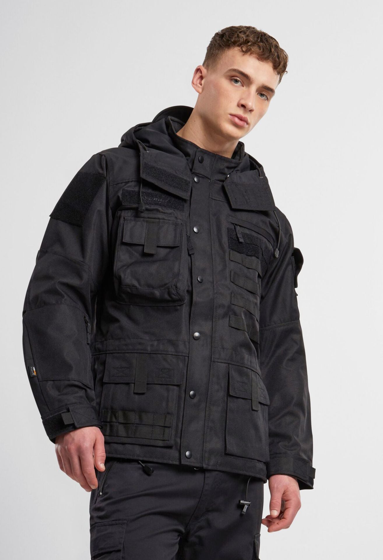 Schwarze Brandit taktische Performance-Jacke aus wasserabweisendem 900D-Polyester mit abnehmbarer Kapuze, verstellbarer Taille und Molle-Bändern