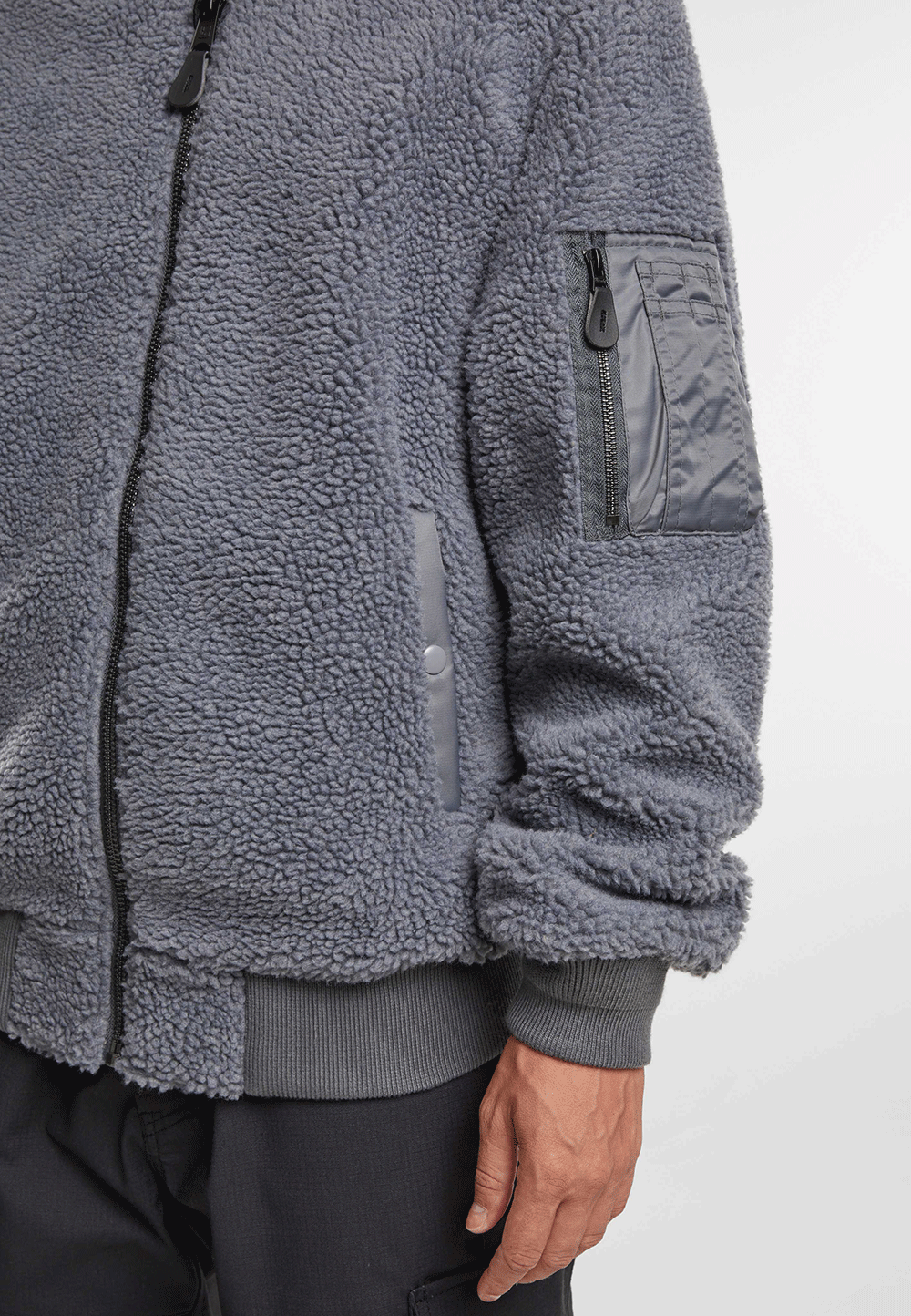 Brandit Teddyfleece-Bomberjacke in Anthra mit Strickbund, zwei Einschubtaschen und Oberarmtasche mit Reissverschluss.