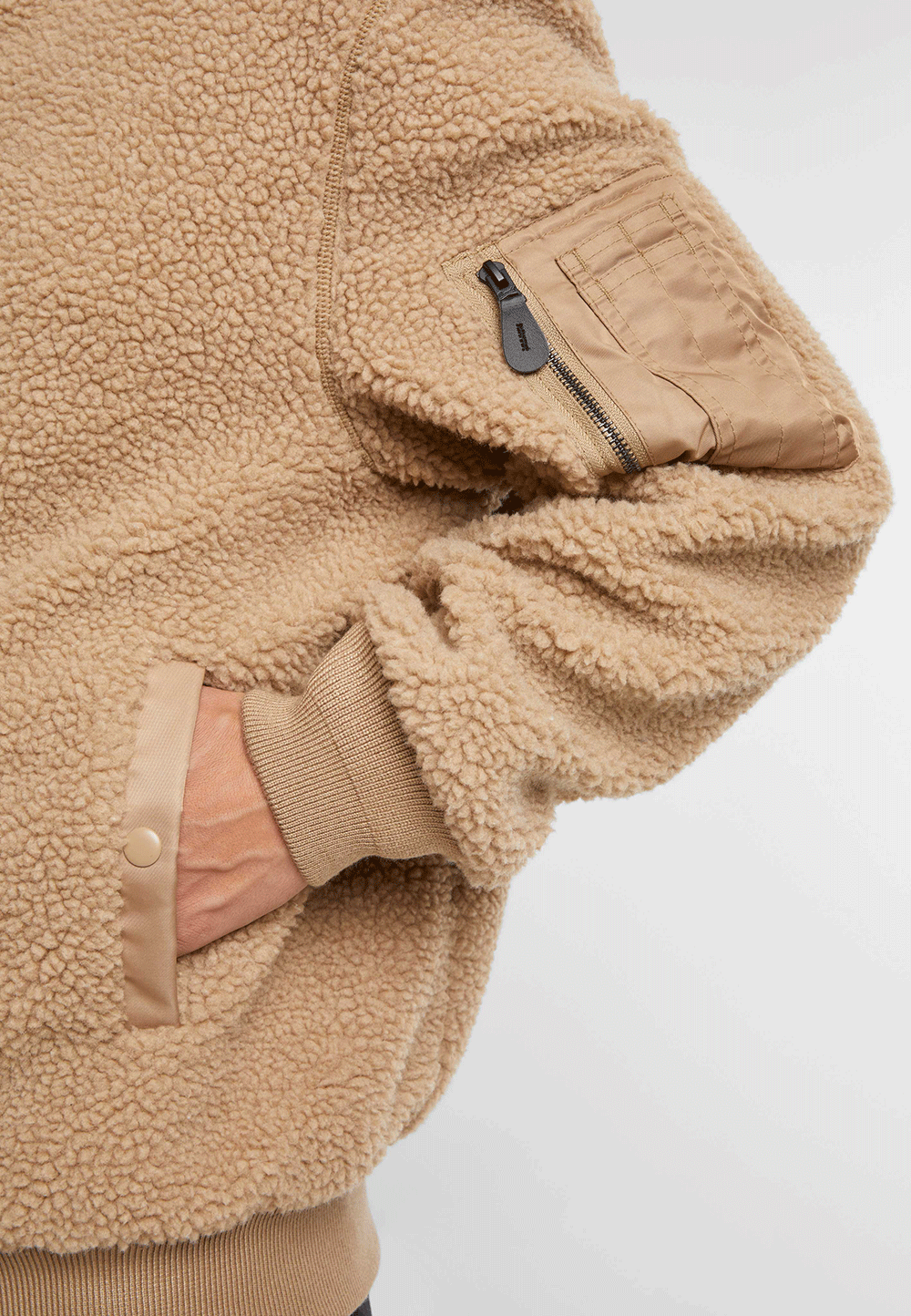 Brandit Teddyfleece-Bomberjacke in Camel mit Strickbund, zwei Einschubtaschen und Oberarmtasche mit Reissverschluss.
