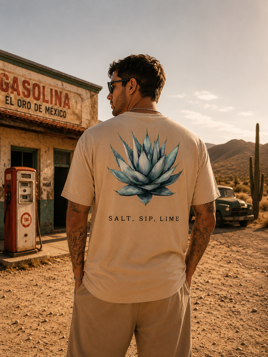 Mann trägt das Mexico Salt Sip Lime Tee in Sand vor einer alten mexikanischen Tankstelle in der Wüste bei Sonnenuntergang mit großem Agave Backprint und Desert-Vibes.