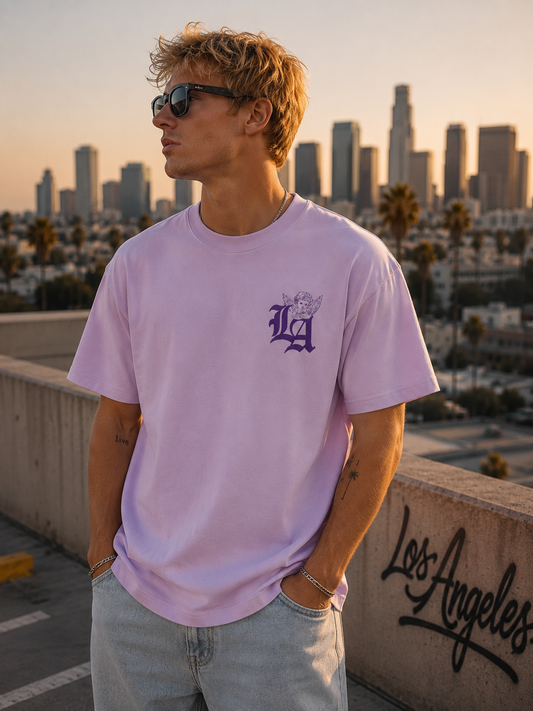 Blonder junger Mann trägt lilacfarbenes Guardian Angel of LA Tee mit Angel Frontprint auf einem Rooftop in Los Angeles bei Sonnenuntergang.