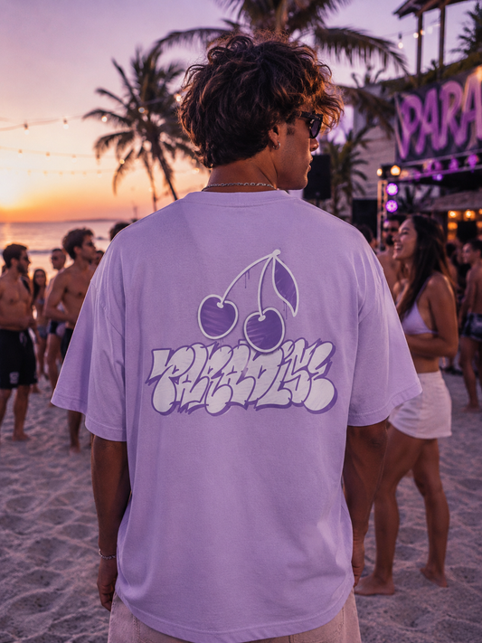 Lifestyle Aufnahme eines Models mit Mister Tee Paradise Cherries Tee in Lavender auf einer sommerlichen Beach Party bei Sonnenuntergang mit urbanem Streetwear Look