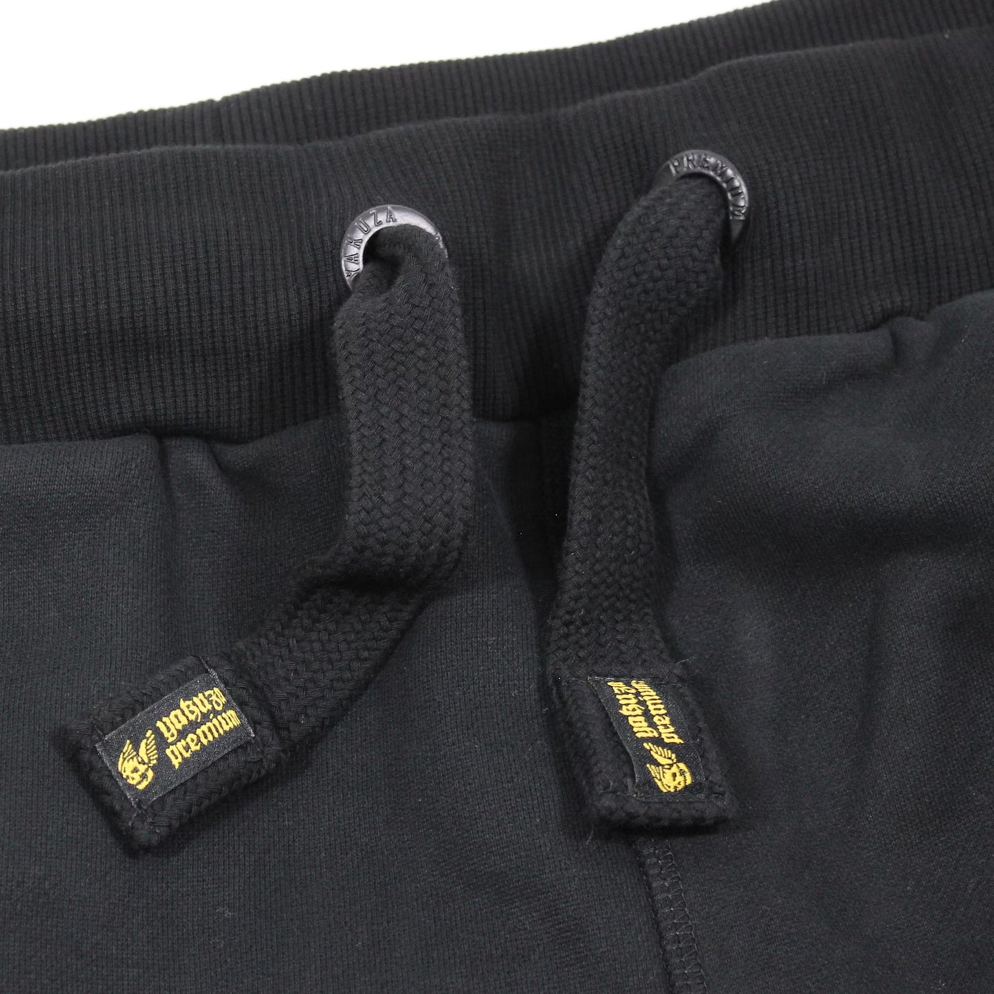 Yakuza Premium Herren Jogginghose Schwarz Detailansicht elastischer Bund mit schwarzen Kordeln und gelb gesticktem Logo-Label.