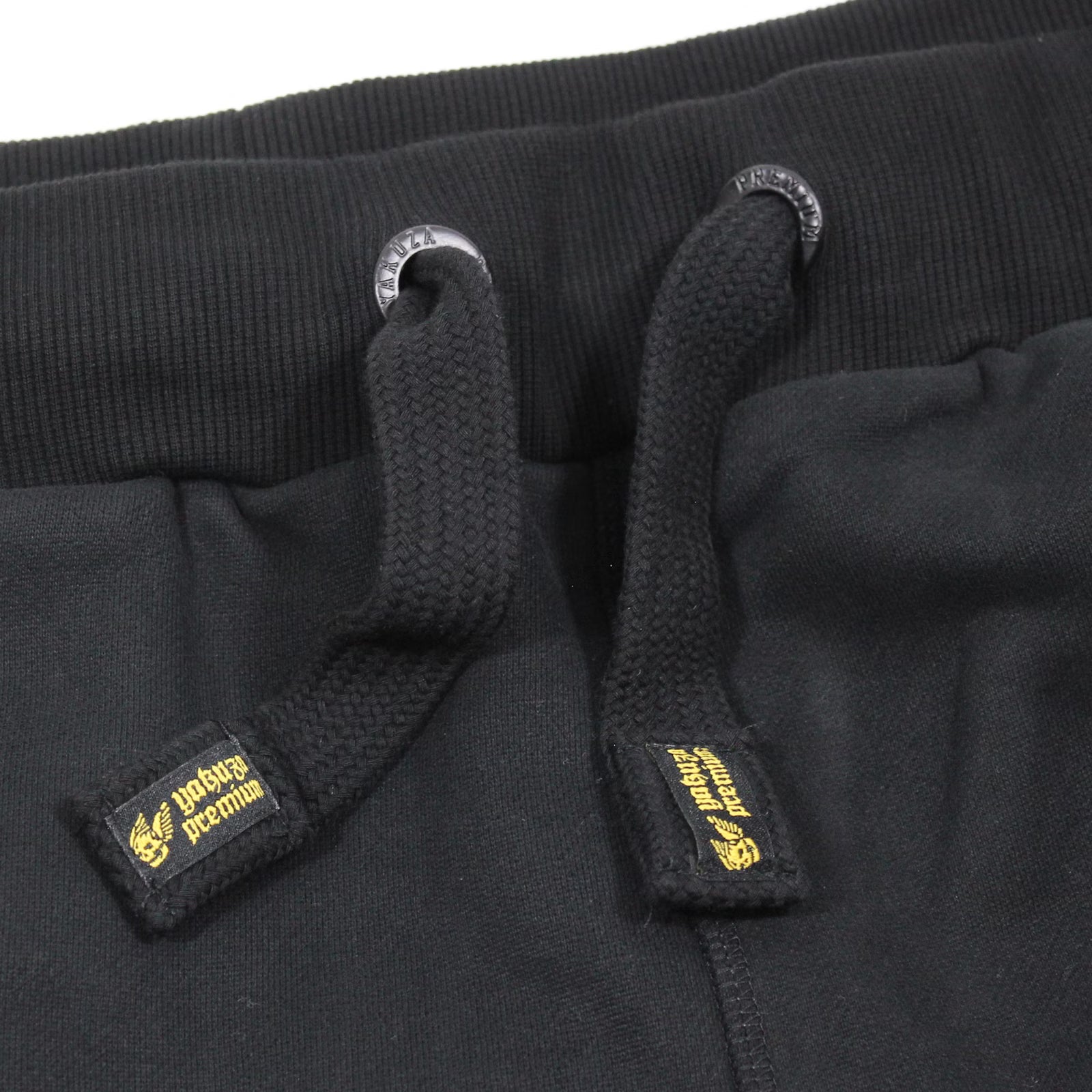 Yakuza Premium Herren Jogginghose Schwarz Detailansicht elastischer Bund mit schwarzen Kordeln und gelb gesticktem Logo-Label.