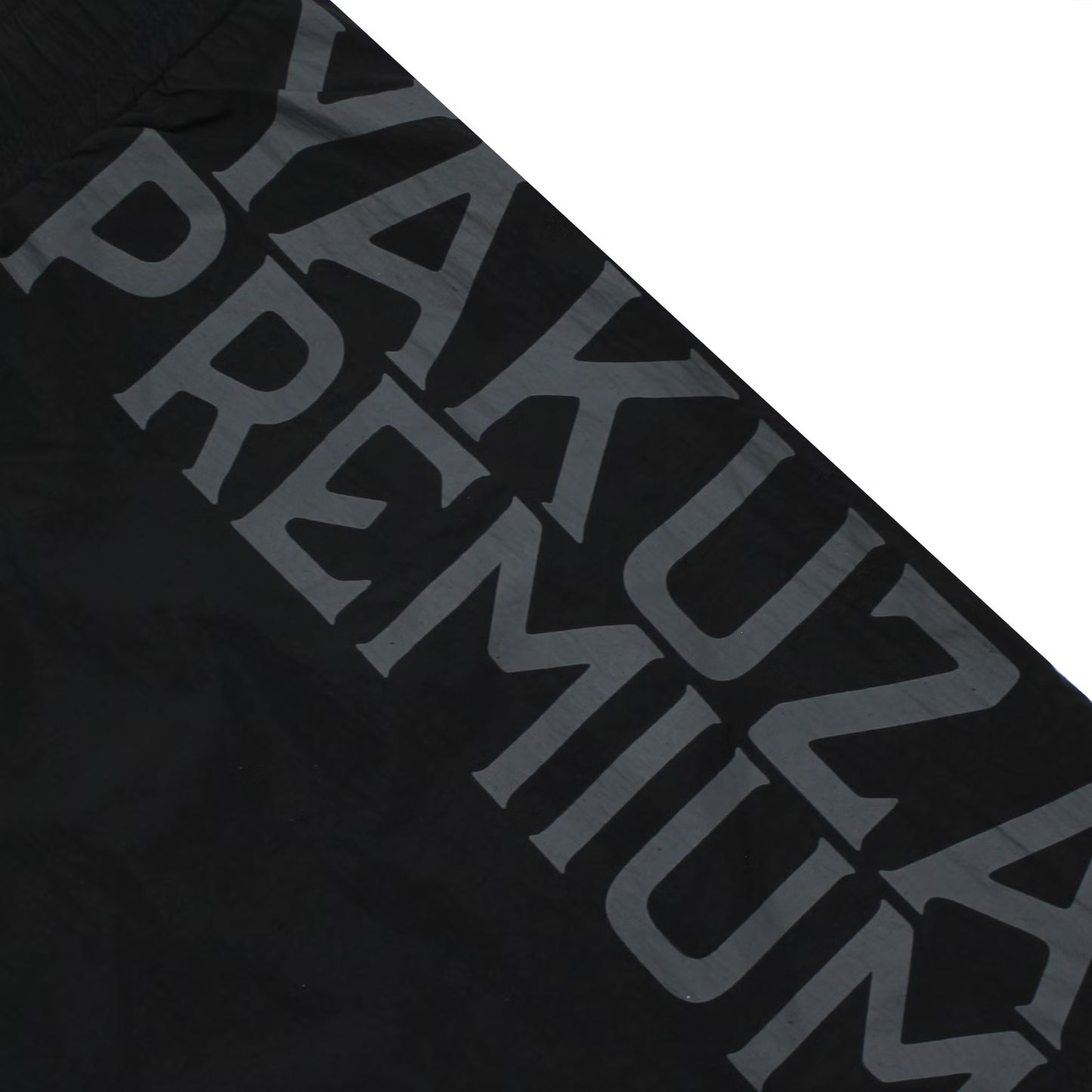 Detailansicht des grauen, vertikalen Yakuza Premium Logo-Schriftzugs auf den schwarzen Badeshorts.