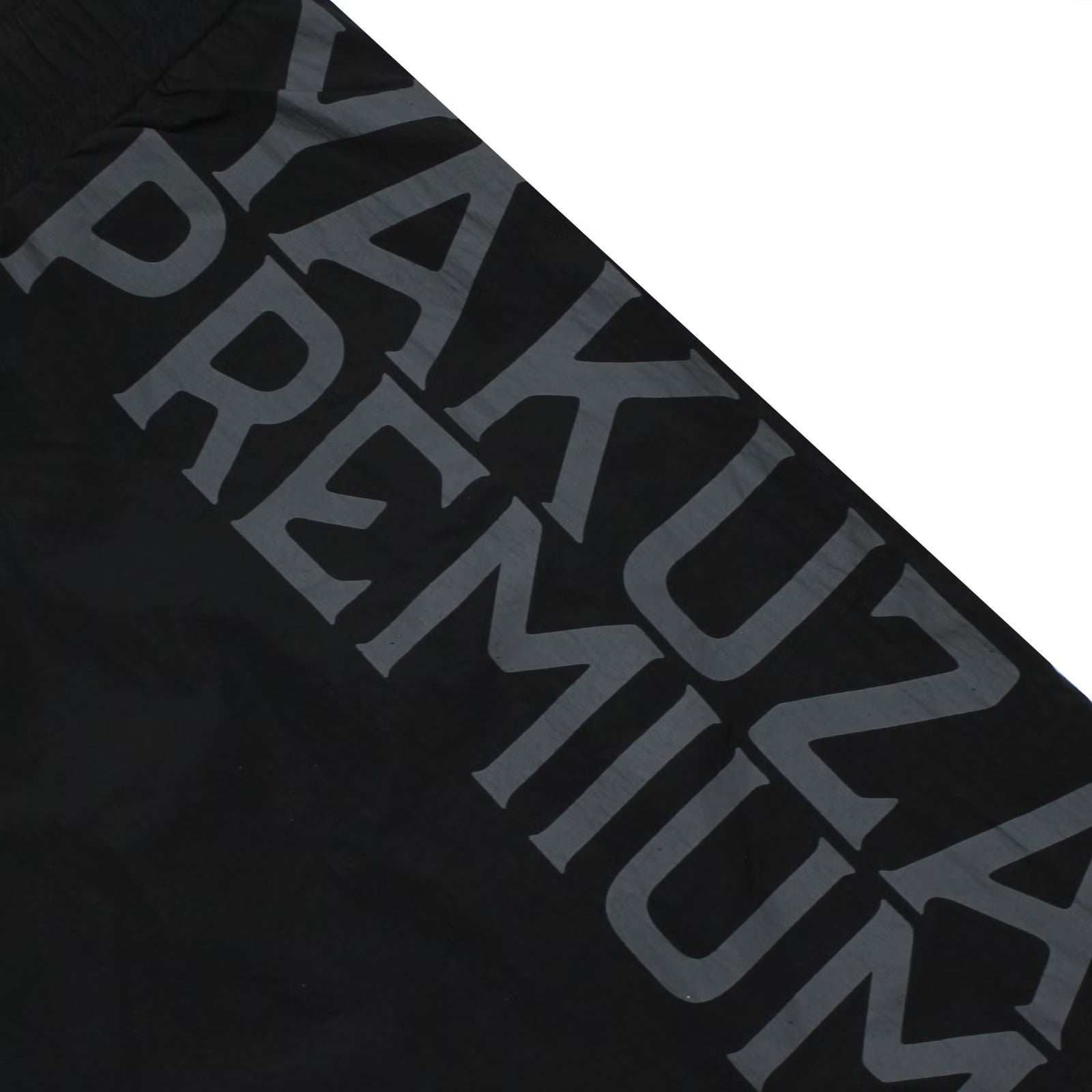 Detailansicht des grauen, vertikalen Yakuza Premium Logo-Schriftzugs auf den schwarzen Badeshorts.